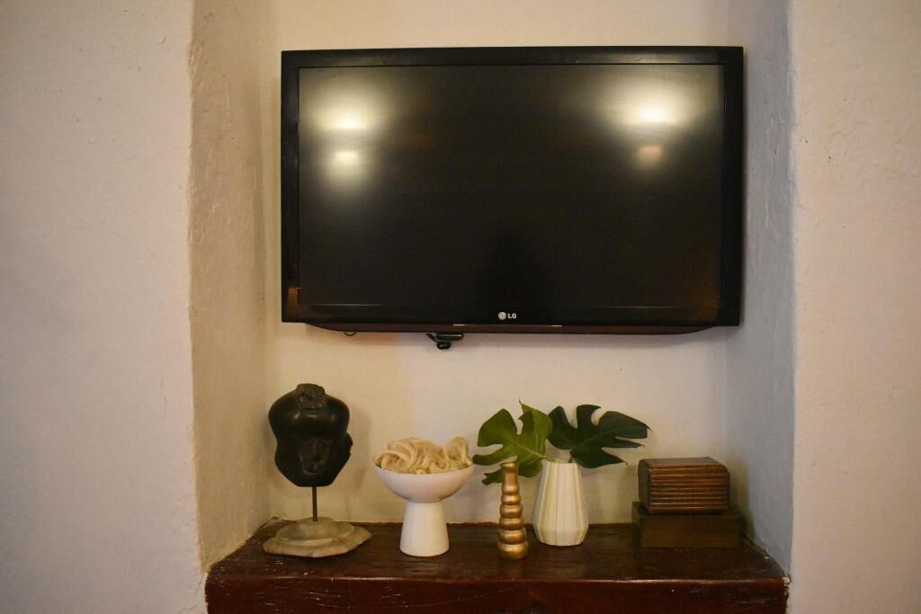 Un téléviseur à écran plat fixé au mur, au-dessus d’une console en bois agrémentée d’objets décoratifs.