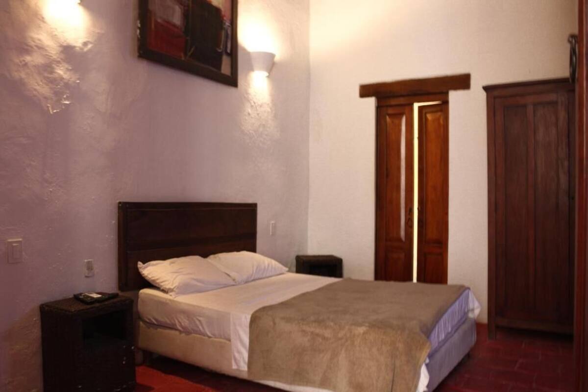 Un dormitorio con una cama individual, una mesita de noche, una lámpara de pared y un armario de madera.