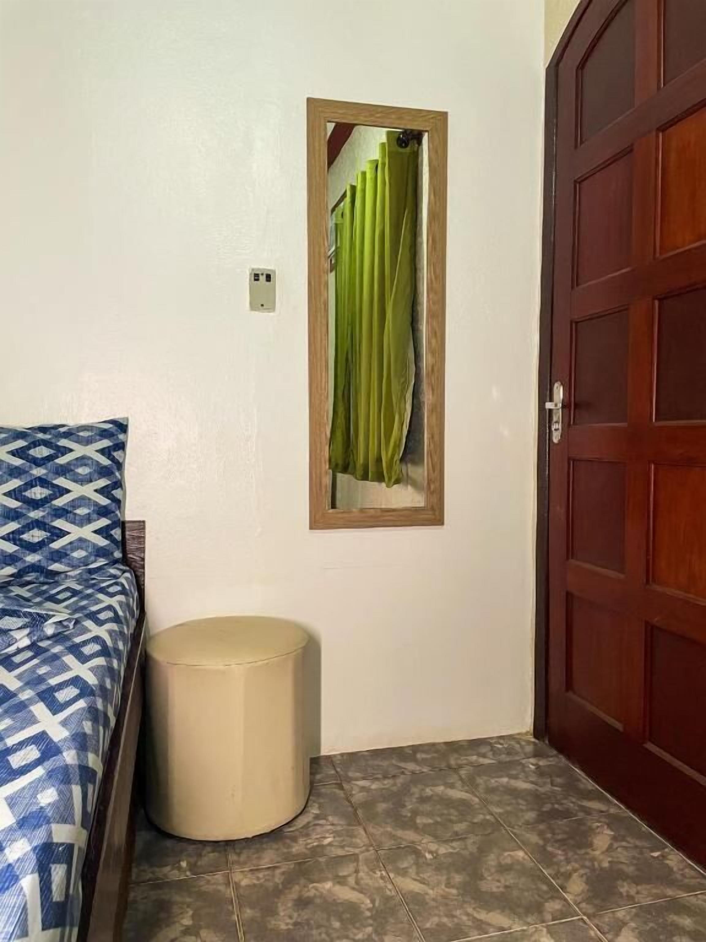 A bedroom with a bed, a small stool, a wooden door, and a mirror with a green curtain.