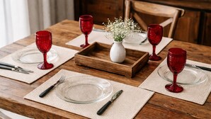 A wooden dining table set with red wine glasses, clear plates, and cutlery on beige placemats. - Light and comfort in Passos, 40 minutes from Capitólio. (Passos)