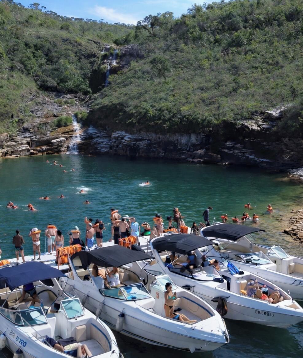 Un port de plaisance avec des bateaux amarrés, des gens qui se baignent dans l’eau et une cascade en arrière-plan.