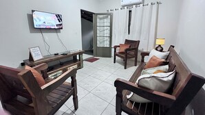 A living room with a television, a wooden table, a sofa, and a chair. - Light and comfort in Passos, 40 minutes from Capitólio. (Passos)