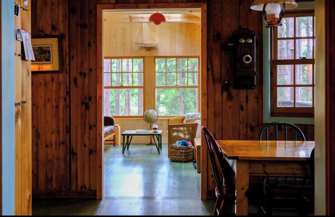 L’intérieur d’un chalet en bois, avec un coin repas, un globe terrestre posé sur une table et une horloge au mur.