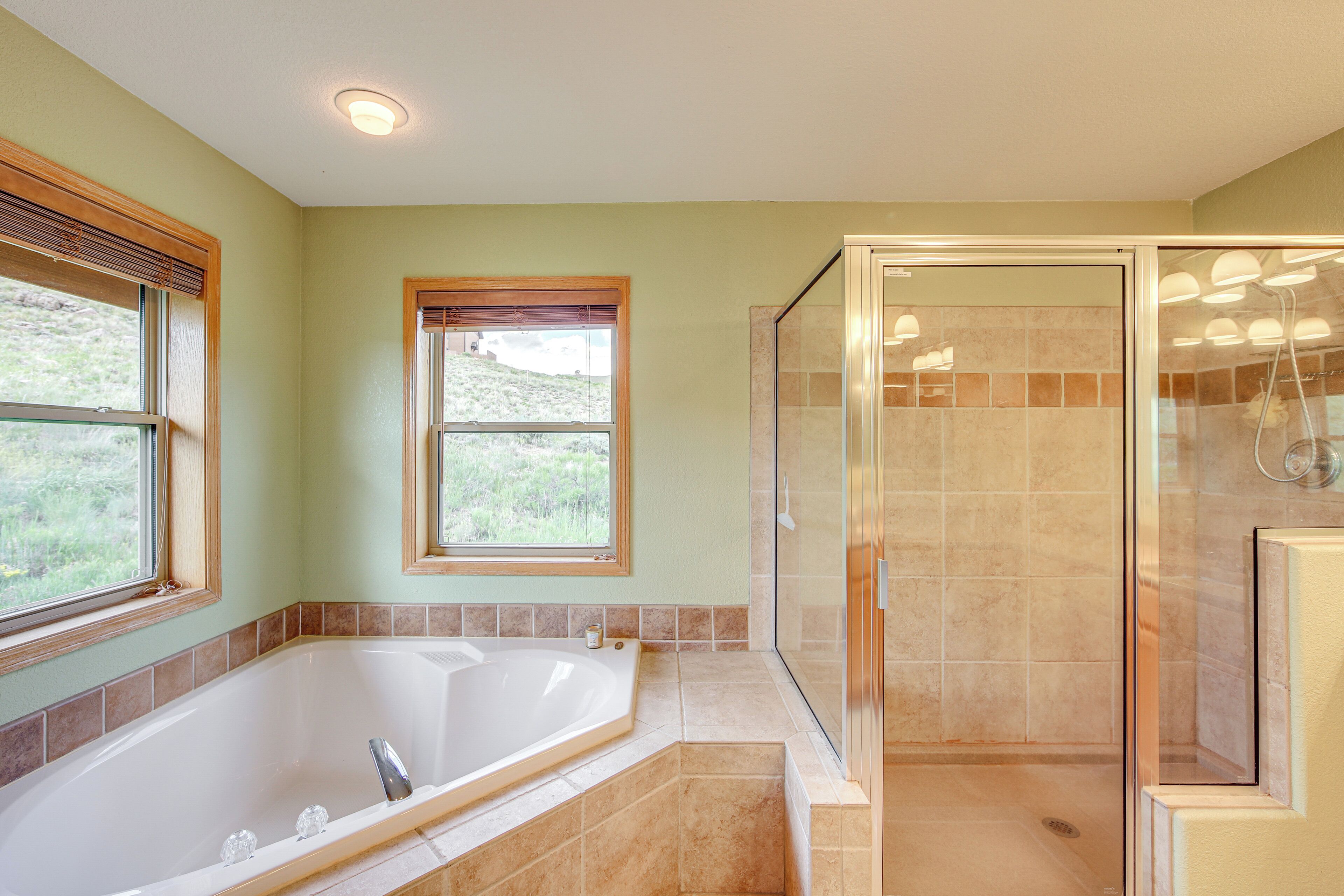 Un baño con una bañera grande, una ducha con paredes de cristal y dos ventanas con marcos de madera.