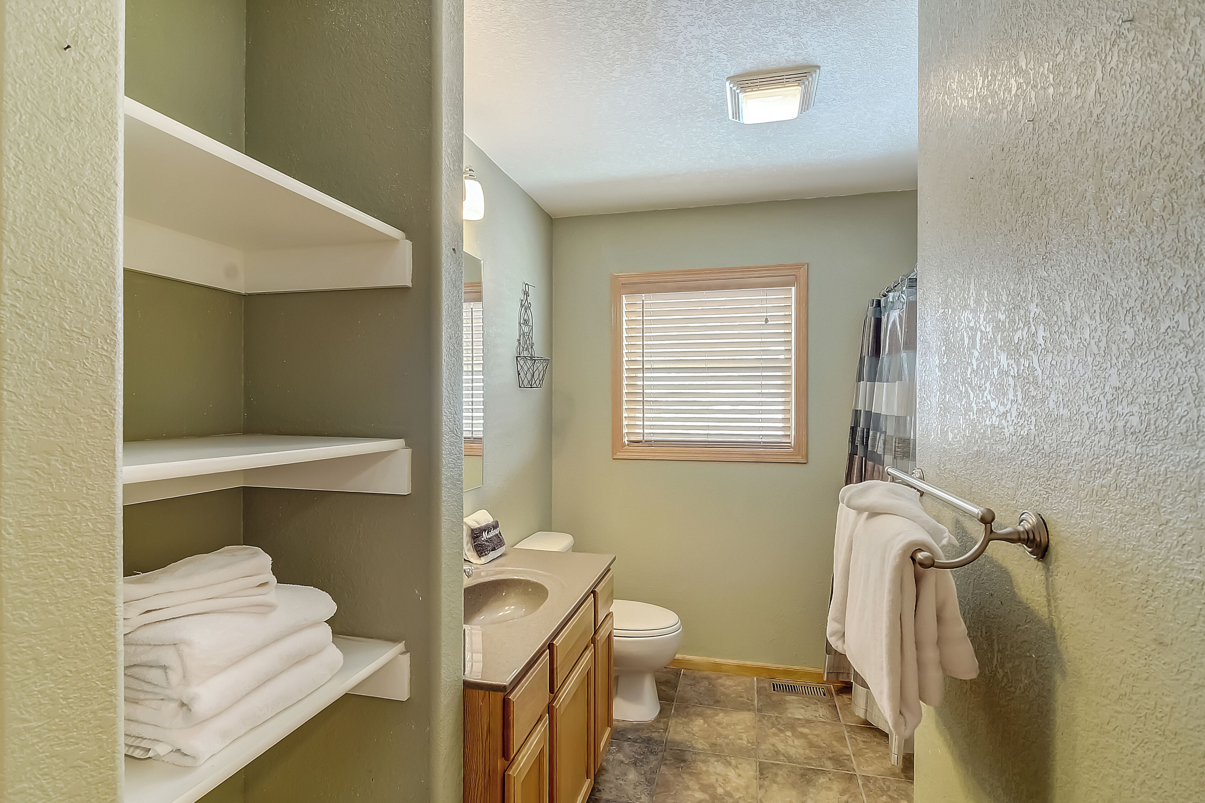 A bathroom with a toilet, sink, and towel rack. Shelves are visible on the left.