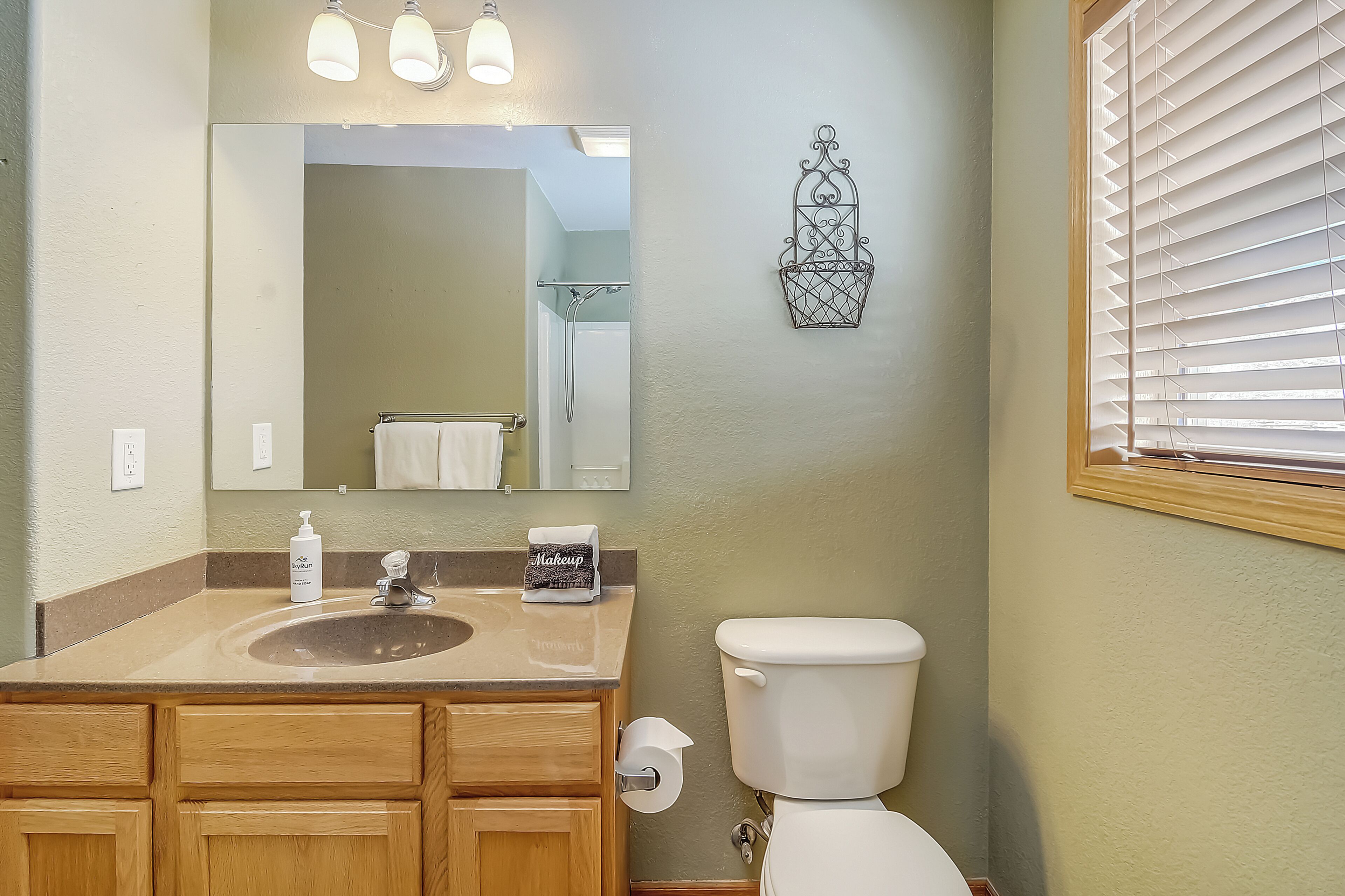 Une salle de bain équipée d’un lavabo, d’un miroir, de toilettes et d’une fenêtre avec des stores.