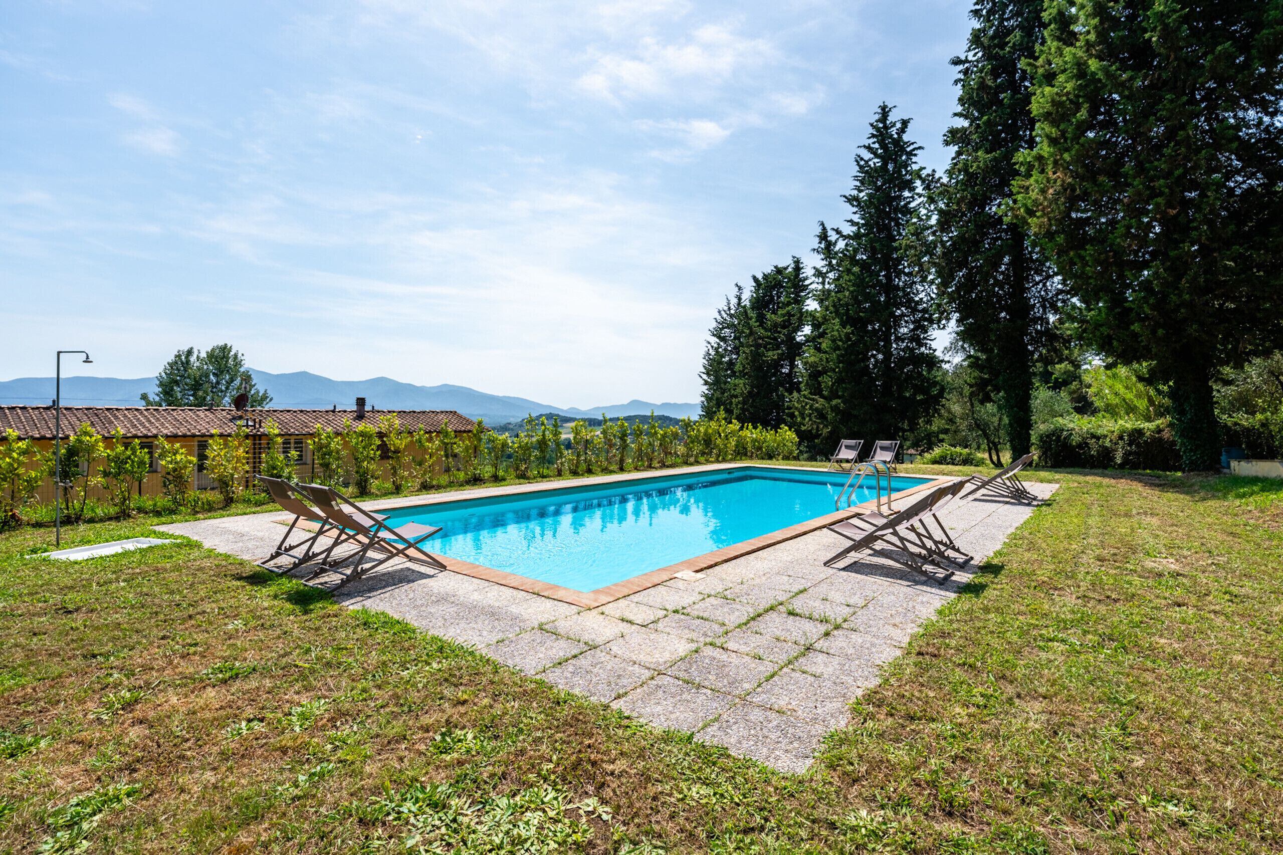 A rectangular swimming pool with two lounge chairs on each side, surrounded by a paved deck.