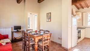A dining area with a wooden table and chairs, a television on a side table, and a kitchen area with cabinets and a refrigerator. - Romeo Apartment with Swimming Pool (Capannori)