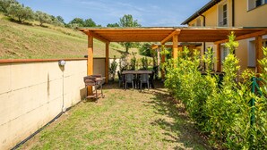 A patio area with a wooden pergola, a table with chairs, and a barbecue grill. - Romeo Apartment with Swimming Pool (Capannori)