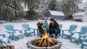 Eine Familie sitzt an einer Feuerstelle, während verschneite Stühle und ein Bauernhof im Hintergrund zu sehen sind.