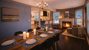 Ein moderner Essbereich mit einem Holztisch, gedeckt für vier Personen, einem Chandelier und einem Kamin im Hintergrund.