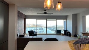 A modern dining area with a white table, two hanging pendant lights, and a view of a marina through large windows. - Casa del mar beach resort (Salsipuedes)