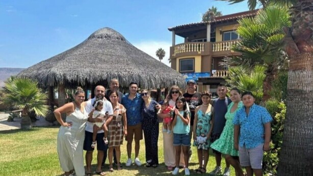 A group of people posing in front of a thatched-roof structure with a building in the background. - Casa del mar beach resort (Salsipuedes)