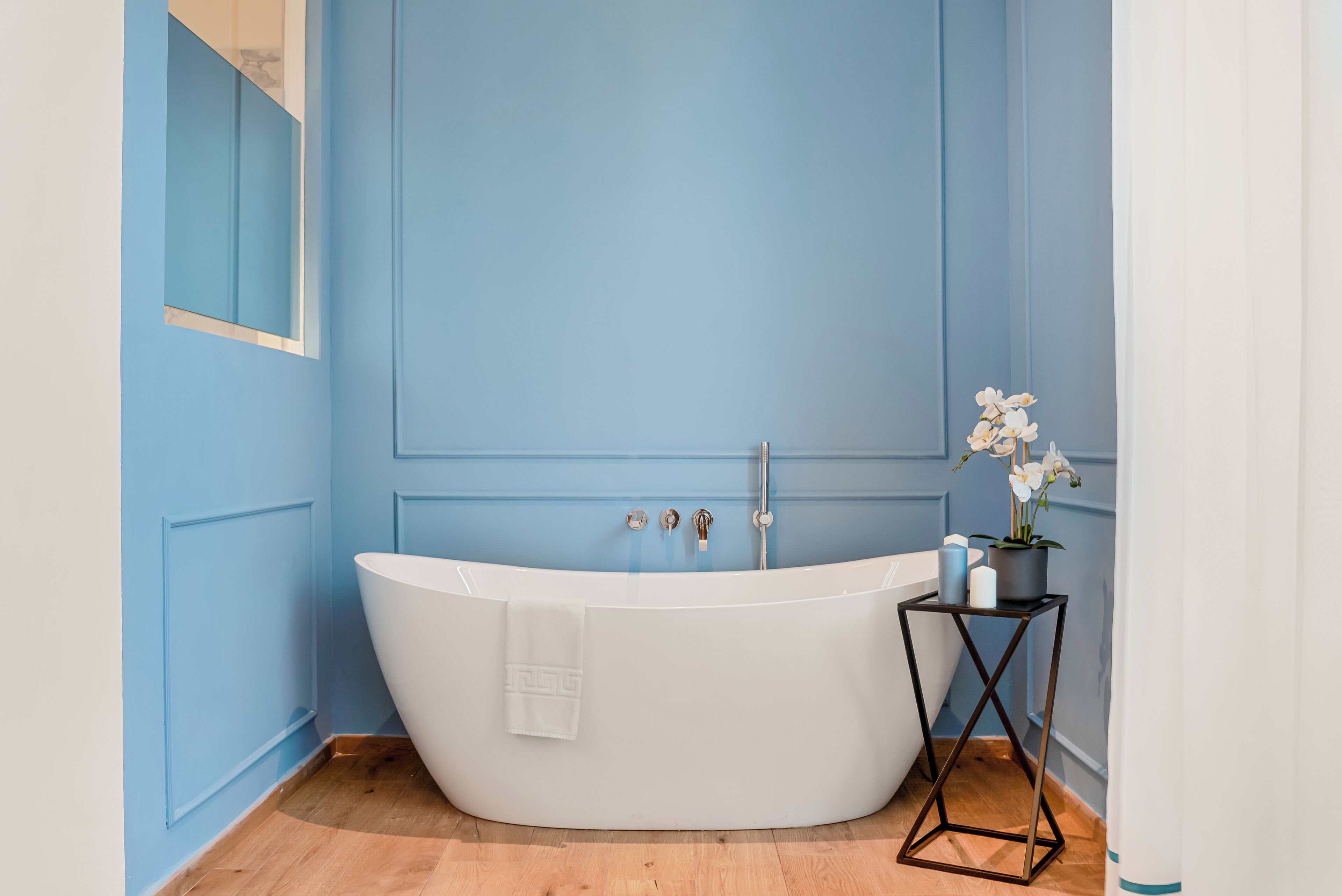 A modern bathroom with a freestanding bathtub, a small table with toiletries, and a mirror on the wall.