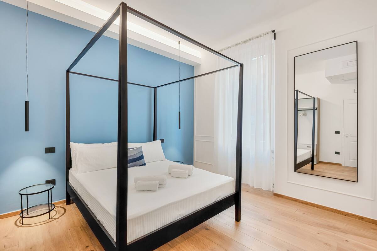 Un dormitorio moderno con cama con dosel, una mesita redonda y un espejo grande en la pared.