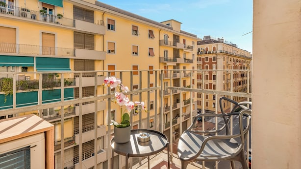 Un balcon avec une table et des chaises, un pot d’orchidée et une vue sur des immeubles à plusieurs étages.