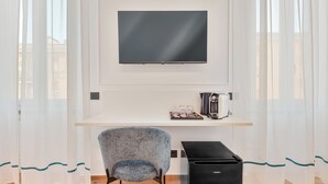 Une chambre moderne équipée d’une télévision murale, d’un petit bureau avec une bouilloire, d’une chaise et d’un meuble noir.