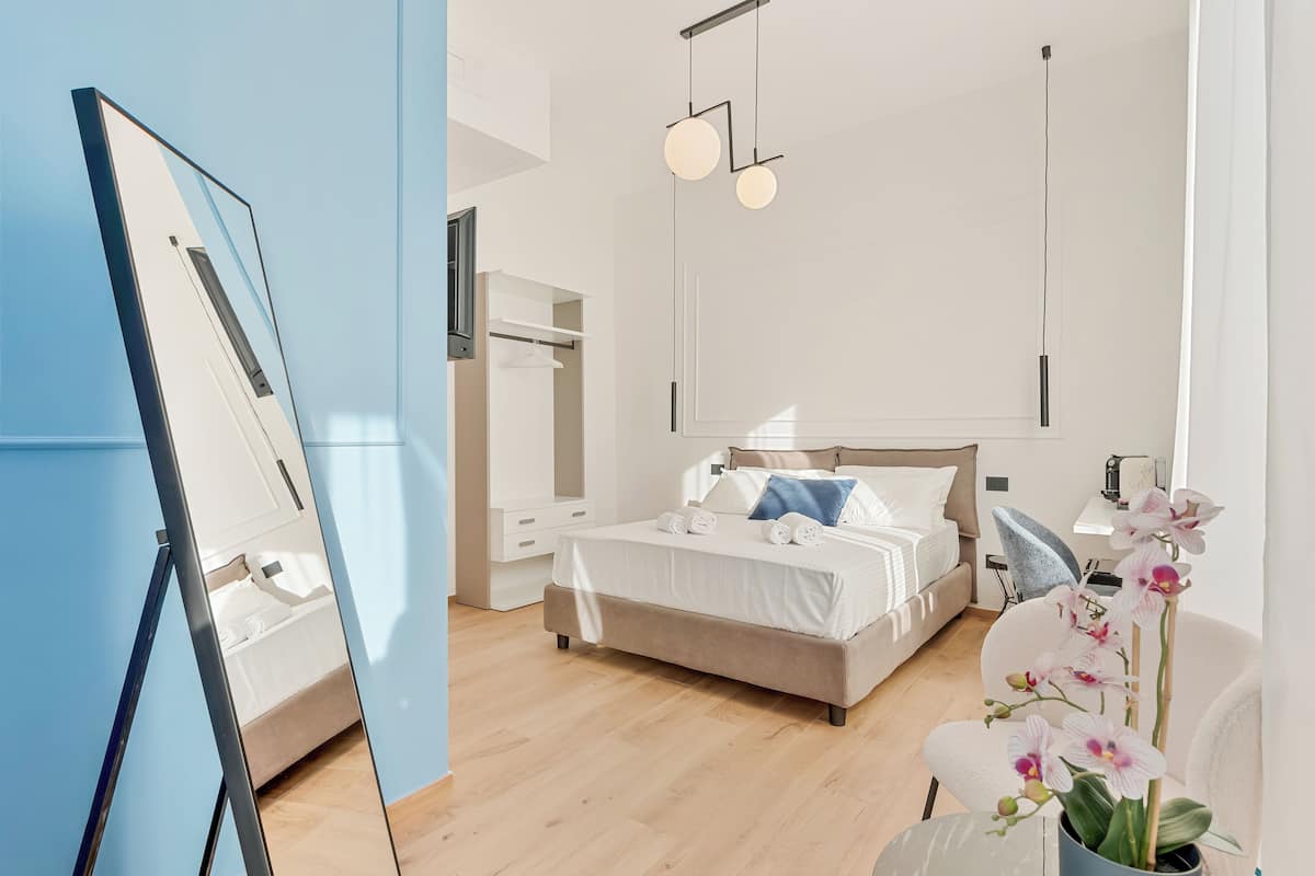 Un dormitorio moderno con cama, mesitas de noche, un espejo y una orquídea en maceta.