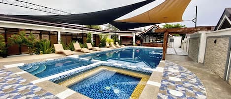 A swimming pool with tiled patterns, lounge chairs, and shaded areas.