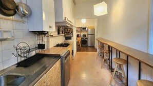 Ett modernt kök med vita skåp, en diskho i rostfritt stål, en mikrovågsugn och en inbyggd ugn. Det finns barstolar vid köksön och en hängande lampa.