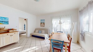 Et værelse med spisebord, stole, sofa, skab og et maleri på væggen.