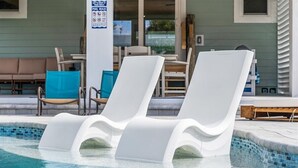 A pool area with two white lounge chairs, a poolside table, and a sign with pool rules. - Private Pool + Backyard + Steps to the Beach (Cocoa Beach)