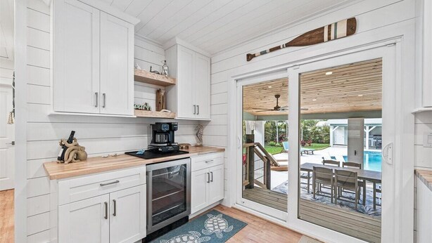 A kitchen with white cabinets, a coffee maker, and a view of an outdoor pool area through a sliding glass door. - Private Pool + Backyard + Steps to the Beach (Cocoa Beach)