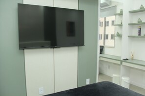 Quarto moderno com televisão de tela plana na parede, mesa preta e prateleira de vidro com objetos decorativos.