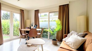 Un salon moderne comprenant un canapé, une table à manger avec des chaises, un téléviseur et de grandes fenêtres avec des rideaux.