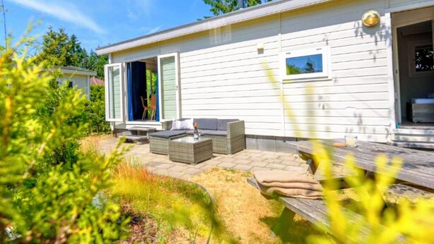 Une maison moderne dotée d’un patio, d’un espace salon extérieur et d’une porte donnant sur une zone abritée.