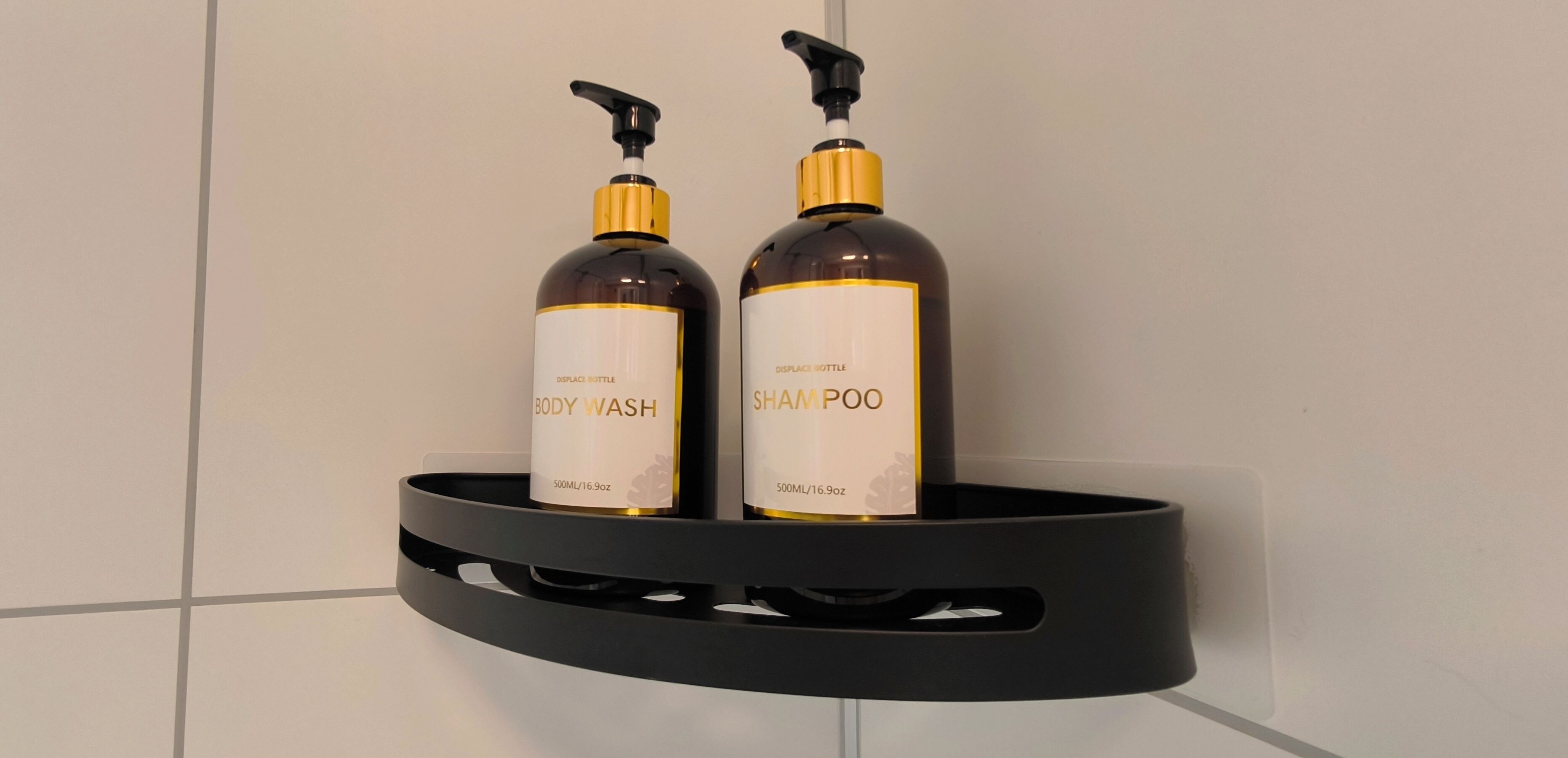 Two bottles of body wash and shampoo on a black shelf against a tiled wall.