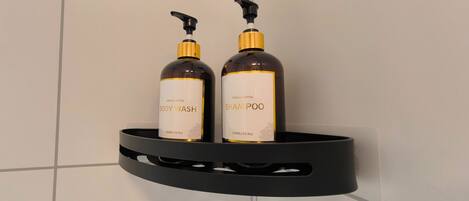 Two bottles of body wash and shampoo on a black shelf against a tiled wall.
