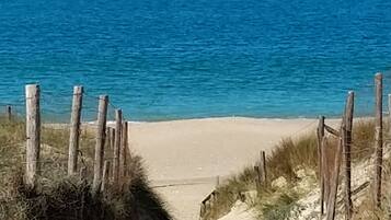 Een pad van zandstrand dat naar de oceaan leidt, afgegrensd door houten palen en begroeiing.