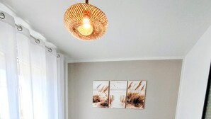 A neatly made bed with a white bedspread, a hanging light fixture, and a wall-mounted artwork. - A little pied-à-terre in Marennes (Marennes-Hiers-Brouage)