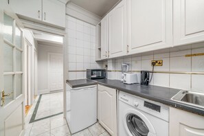 Een kleine keuken met witte kasten, een magnetron, een broodrooster en een wasmachine.