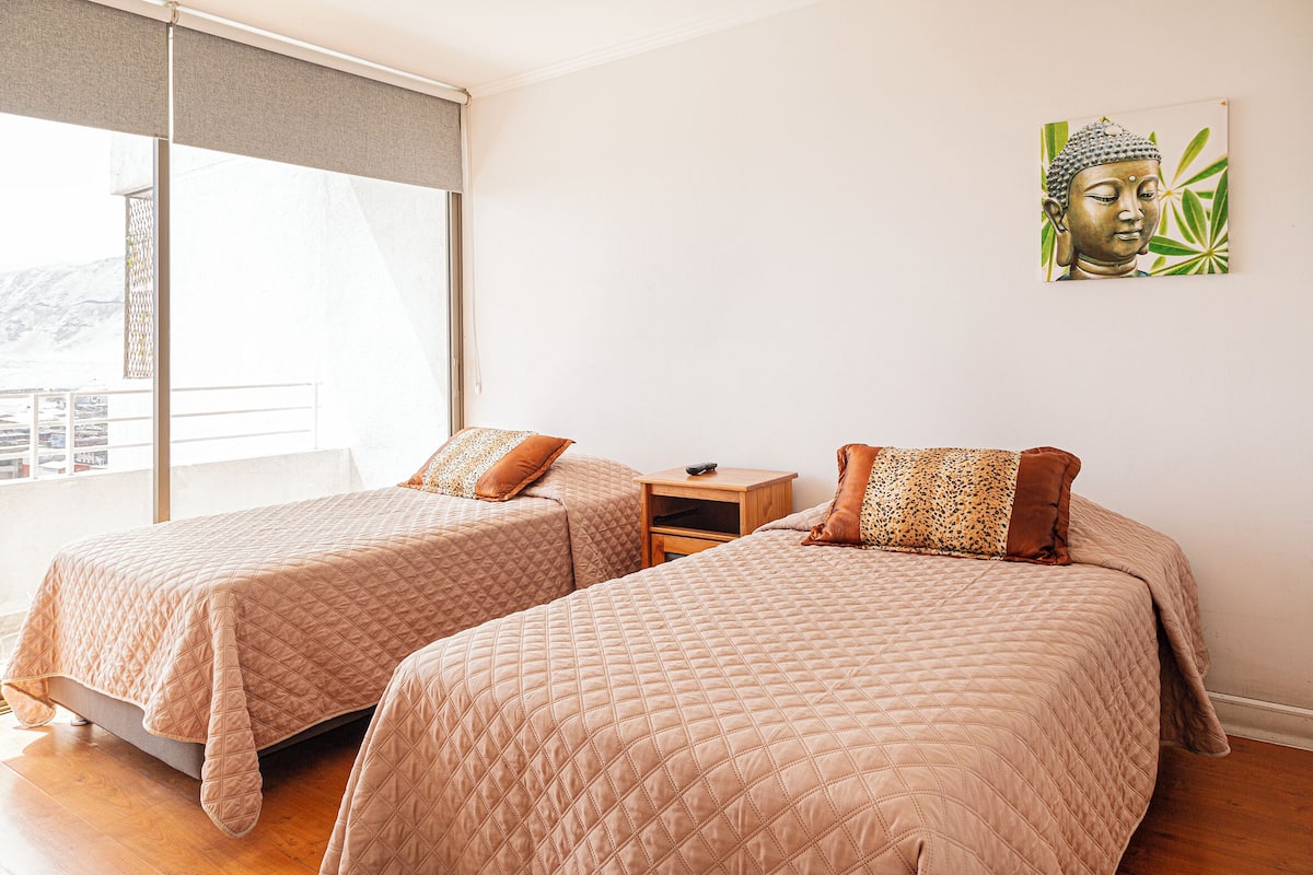 A bedroom with two beds, a nightstand, and a window with a view.