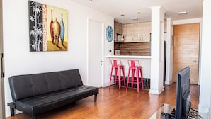 A modern living room with a black sofa, a TV, and a painting on the wall.