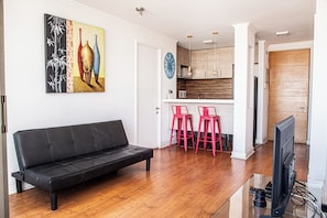 A modern living room with a black sofa, a TV, and a painting on the wall. - Depto Suite Centro Iquique (Iquique)