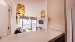 Una cocina moderna con una isla grande, luces colgantes, un televisor de pantalla plana y vistas a la ciudad a través de amplios ventanales.