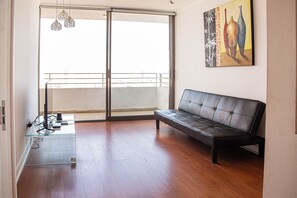 Ein Zimmer mit einer Schiebeglastür, die auf einen Balkon führt, einem schwarzen Ledersofa und einem Glastisch mit einer Fernbedienung darauf.