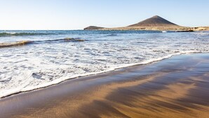 Ein Strand mit Wellen, einem sandigen Ufer und einem Berg im Hintergrund.