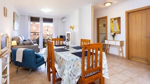Ein Wohnzimmer mit einer Couch, einem Esstisch mit Stühlen, einem Fernseher und einem Balkon mit Blick.