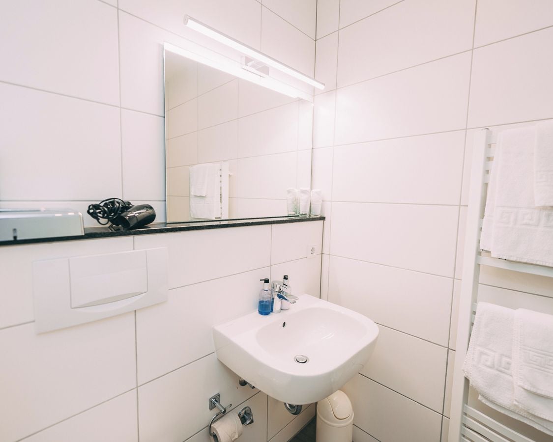 A modern bathroom with white tiles, a white sink, a mirror, and a towel rack.