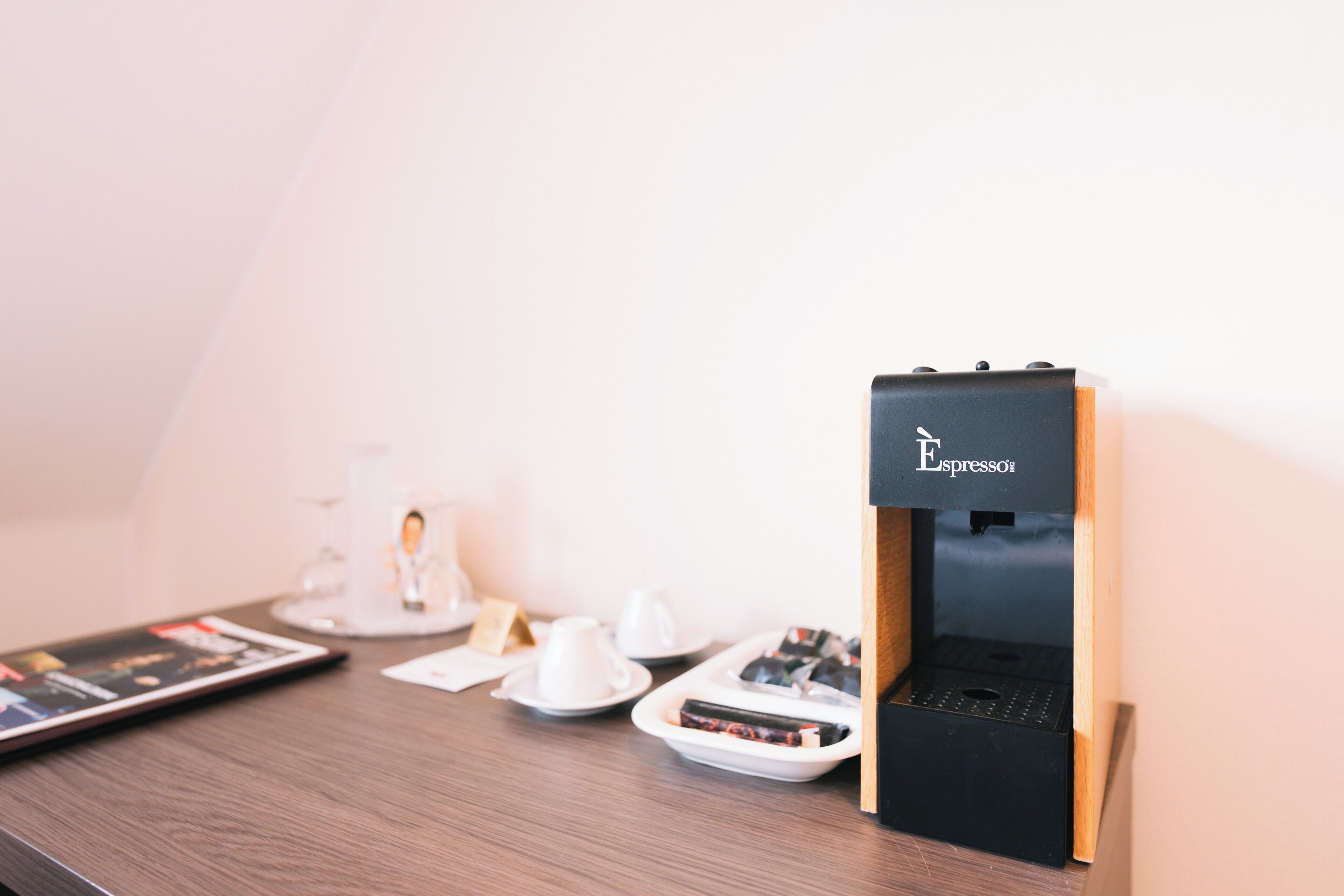 Une machine à café posée sur un support en bois, avec un mur blanc en arrière-plan.