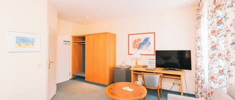 A hotel room with a bed, a round wooden table, a desk with a computer, a TV, and a chair.