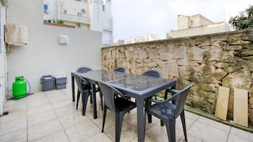 En udendørs terrasse med et bord, stole, en stenvæg og en grøn gasflaske.