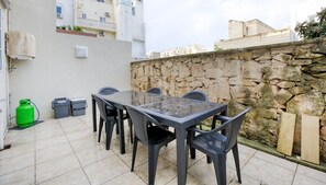 Een terras buiten met een tafel en stoelen, een stenen muur en een groene gasfles.