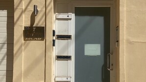 A beige building with a white door, a mailbox, and a small step leading to the entrance. - BELAIR (St. Julian's)