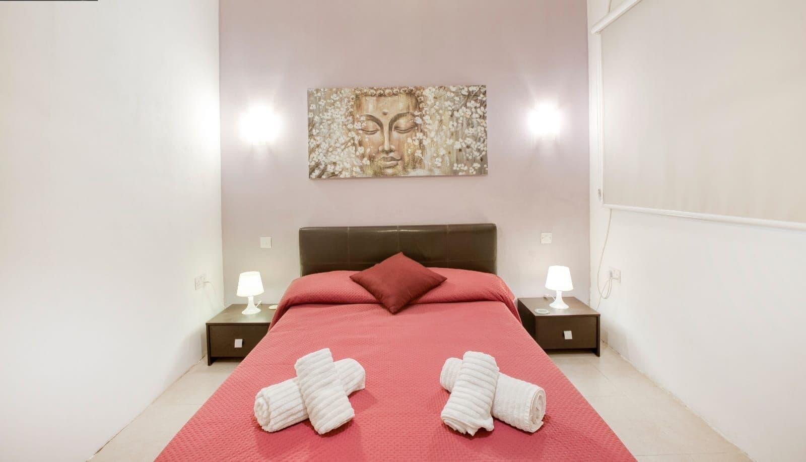 A hotel room with a bed, two bedside tables with lamps, a wall-mounted artwork, and towels on the bed.