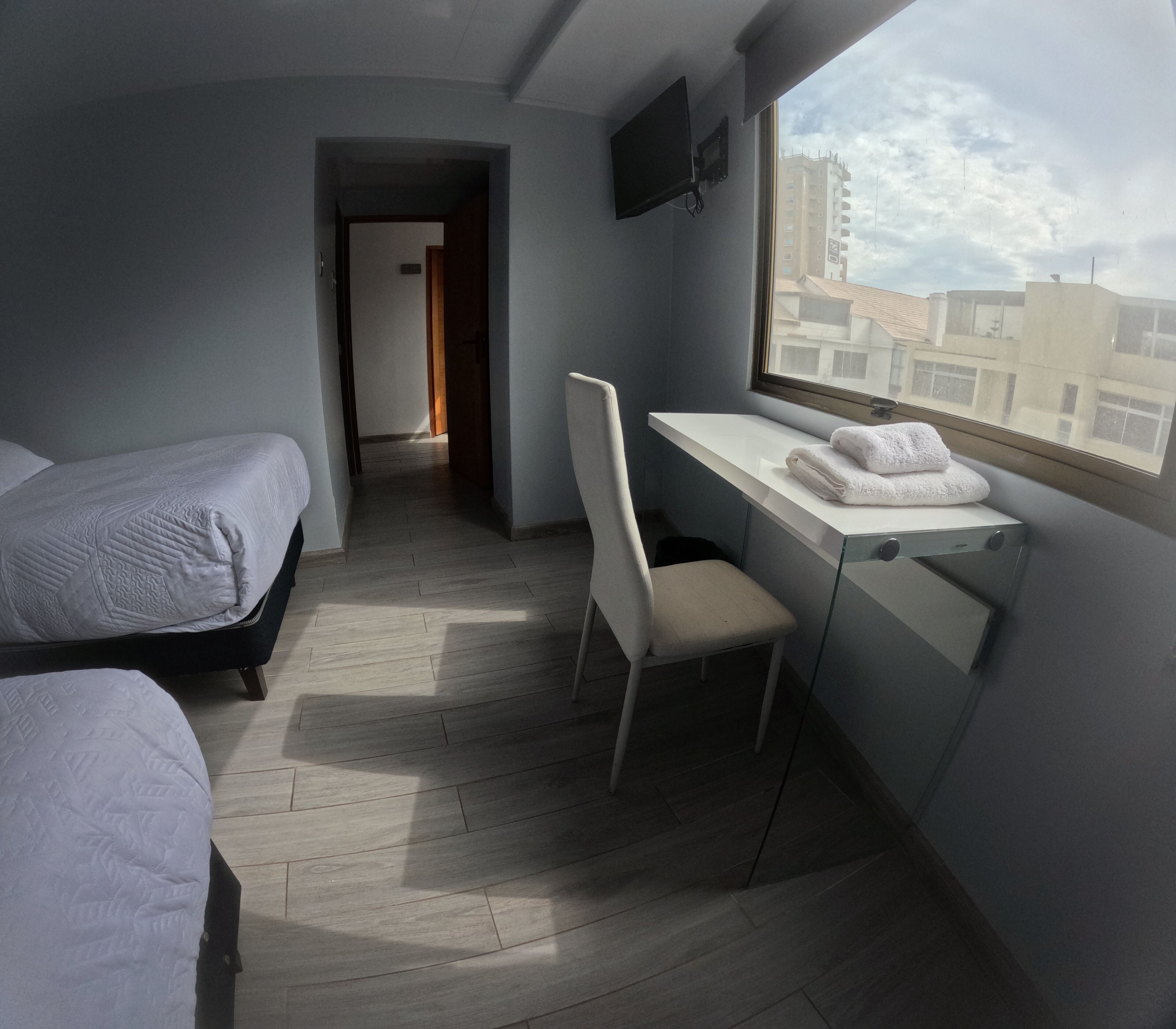 A hotel room with a bed, a desk, a chair, and a window with a view of buildings.